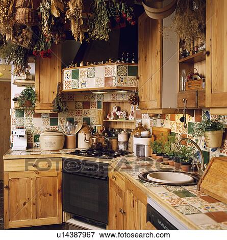 Stock Photo - Dried flowers on ceiling of kitchen with floral patterned tiles and corner oven with sink built into floral tiled worktops . Fotosearch