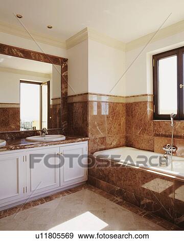 Earth coloured marble tiles above bath and on bath surround in modern neutral bathroom View Large Photo Image Stock Photo - Earth coloured marble tiles above bath and on bath surround in modern neutral bathroom. Fotosearch
