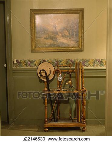 Stock Image - Edwardian umbrella stand in hall with wallpaper border above panelled green dado. Fotosearch
