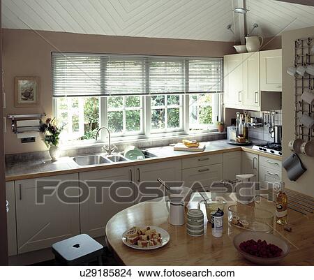 Picture - Electric whisk and cookery ingredients on table in modern table with slatted blinds above sink in white fitted cupboards. Fotosearch