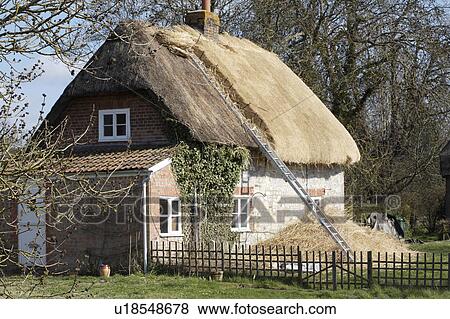Stock Photo - English country cottage with the roof in the process of being re-thatched. Fotosearch