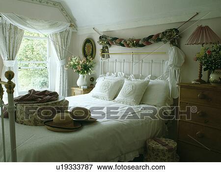 Stock Photo - Fabric garland above white wrought-iron and brass bed with hatbox and hats on the bed. Fotosearch