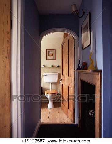 Stock Photo - Fireplace in blue bathroom with arched pine door open to seperate toilet with wooden floor. Fotosearch