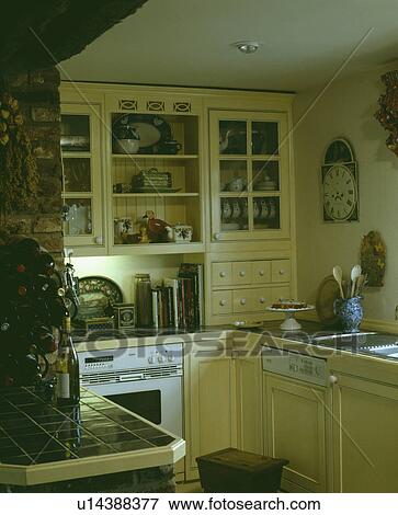 Stock Photo - Fitted dishwasher and white oven in small yellow cottage kitchen with green tiled worktops. Fotosearch