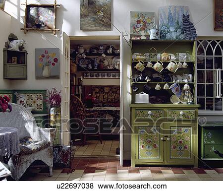 Floral decoration painted on small green dresser in cottage kitchen with white wicker chair beside open internal door View Large Photo Image Stock Photo - Floral decoration painted on small green dresser in cottage kitchen with white wicker chair beside open internal door. Fotosearch