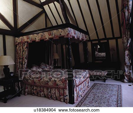Picture - Floral drapes and bedcover on carved wood four-poster bed in country bedroom with beamed apex ceiling. Fotosearch