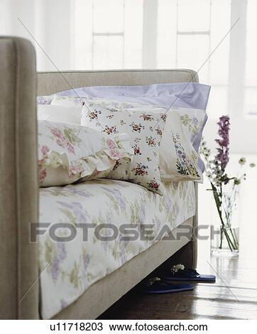 Stock Image - Floral pillows and linen on upholstered grey bed. Fotosearch