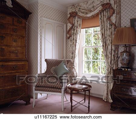 Floral swagged and tailed curtains and peach blind on sash window in country bedroom with armchair beside tray-table View Large Photo Image Stock Photography - Floral swagged and tailed curtains and peach blind on sash window in country bedroom with armchair beside tray-table. Fotosearch