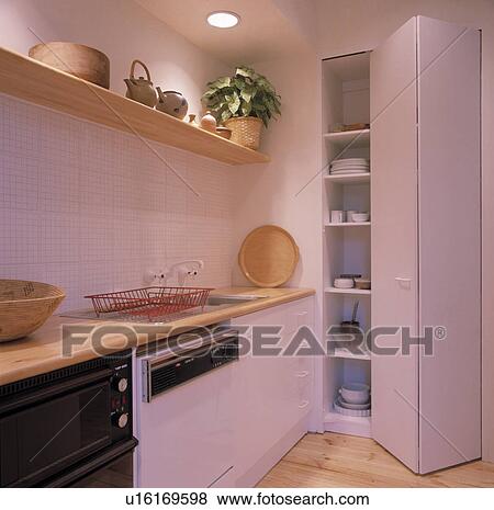Folding door open onto crockery on shelves in modern white kitchen with wooden shelf above fitted sink and dishwasher View Large Photo Image Stock Photo - Folding door open onto crockery on shelves in modern white kitchen with wooden shelf above fitted sink and dishwasher. Fotosearch