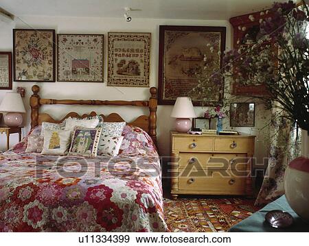 Framed antique samplers behind bed with patchwork quilt in country bedroom with pine chest of drawers View Large Photo Image Stock Photo - Framed antique samplers behind bed with patchwork quilt in country bedroom with pine chest of drawers . Fotosearch