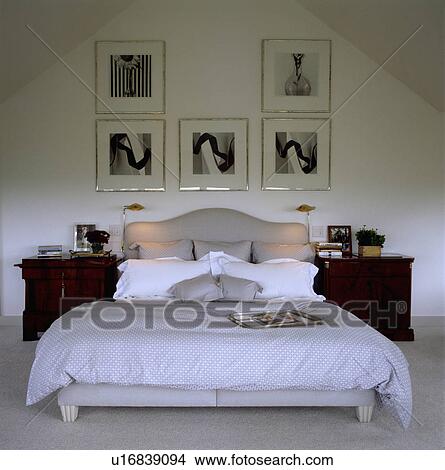 Framed black+white photographs above grey upholstered bed with white pillows with grey linen in modern bedroom View Large Photo Image Picture - Framed black+white photographs above grey upholstered bed with white pillows with grey linen in modern bedroom. Fotosearch