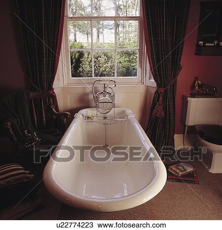 Freestanding rolltop bath in front of sash window with dark red curtains in red bathroom View Large Photo Image Stock Image - Freestanding rolltop bath in front of sash window with dark red curtains in red bathroom. Fotosearch