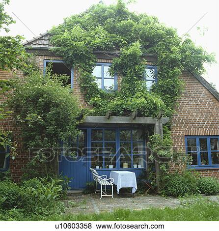 Furniture on patio in front of brick country house with green climber and blue door View Large Photo Image Stock Photo - Furniture on patio in front of brick country house with green climber and blue door. Fotosearch