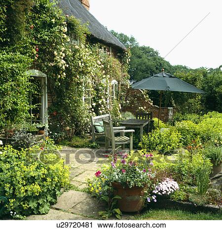 Stock Image - Furniture on patio in summer garden in front of country house. Fotosearch