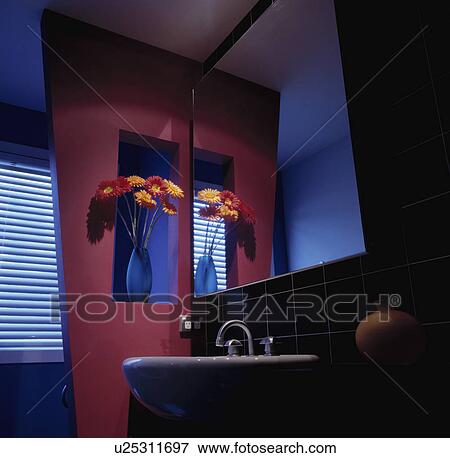 Stock Photo - Gerberas in vase in alcove in red wall beside large mirror above basin. Fotosearch