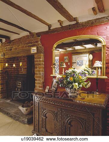 Gilt mirror above carved wooden cupboard in red living room with black iron stove in fireplace View Large Photo Image Stock Image - Gilt mirror above carved wooden cupboard in red living room with black iron stove in fireplace. Fotosearch