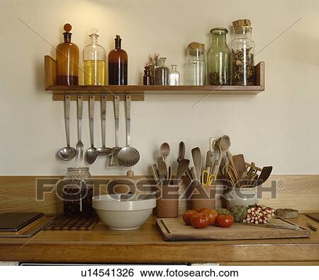 Stock Photograph - Glass bottles on wooden shelf above wooden worktop with utensils in pottery jars. Fotosearch