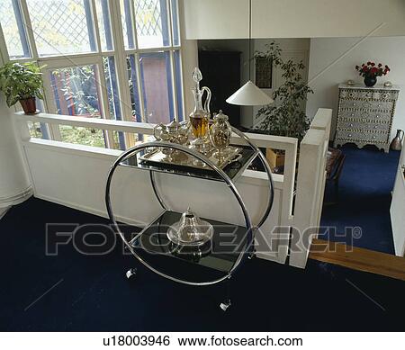 Stock Photograph - Glass decanter and silver teapot on Art Deco chrome and glass table on landing. Fotosearch