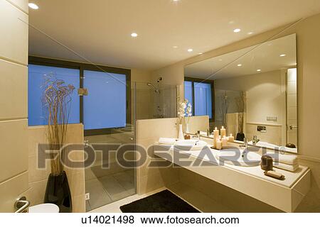 Stock Photo - Glass doors to shower area in modern neutral bathroom with large mirror over double basins. Fotosearch