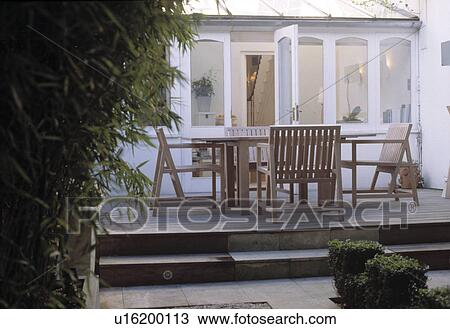 Stock Image - Glass extension leads onto patio with table and chairs in small urban garden.. Fotosearch