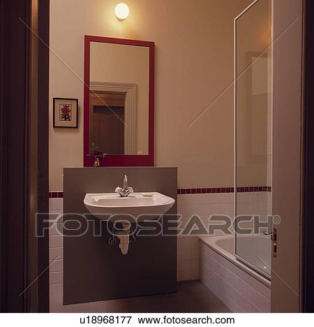 Globe light and red mirror above wall-mounted basin in small modern bathroom View Large Photo Image Stock Photo - Globe light and red mirror above wall-mounted basin in small modern bathroom. Fotosearch