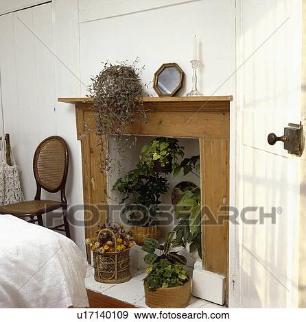 Stock Photo - Green houseplants in old pine fireplace in small white bedroom. Fotosearch