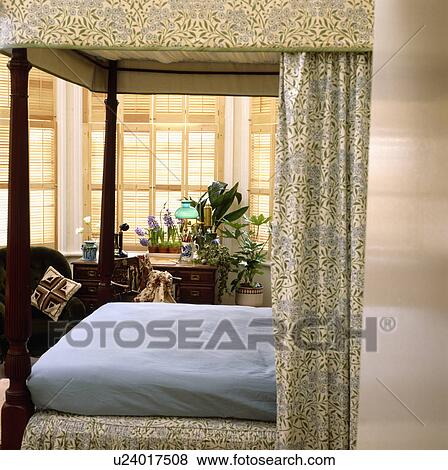 Green+white drapes and blue linen on four-poster bed with plantation shutters at window View Large Photo Image Stock Photo - Green+white drapes and blue linen on four-poster bed with plantation shutters at window. Fotosearch