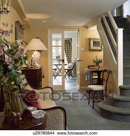 Picture - Grey carpet in country hall with lighted lamp on chest of drawers and glazed doors open to dining room. Fotosearch