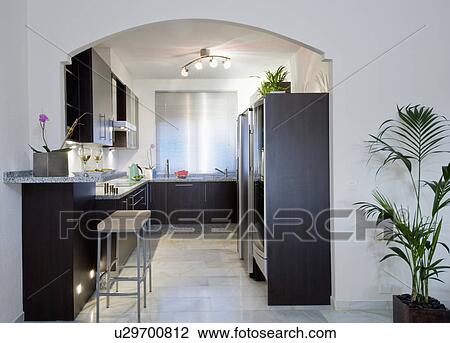 Stock Image - Grey tiled flooring in modern black and white galley kitchen with halogen lighting. Fotosearch