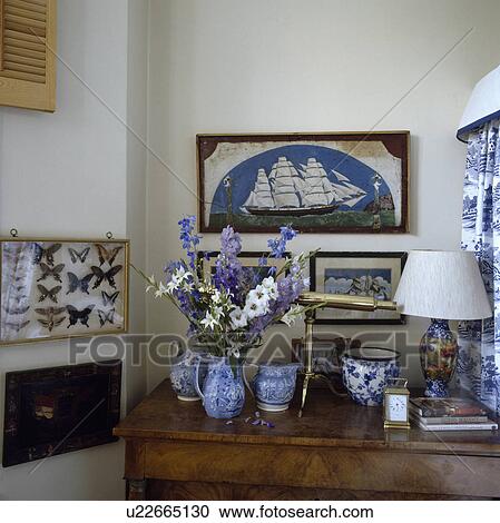 Stock Image - Group of pictures on wall above blue+white jugs on table. Fotosearch