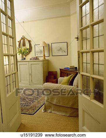 Stock Photo - Half-glazed double doors open to cream livingroom with cream sofa and patterned rug on sisal carpet. Fotosearch