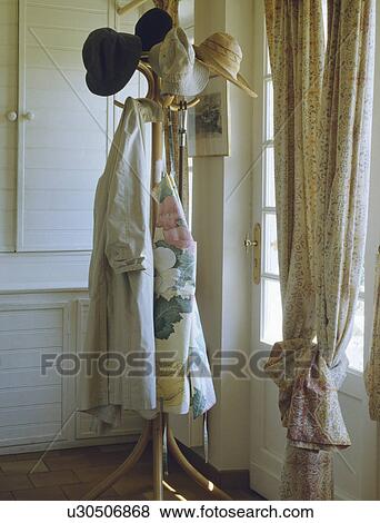 Stock Photo - Hats and coats on bamboo coatstand beside door with neutral curtain in corner of hall. Fotosearch