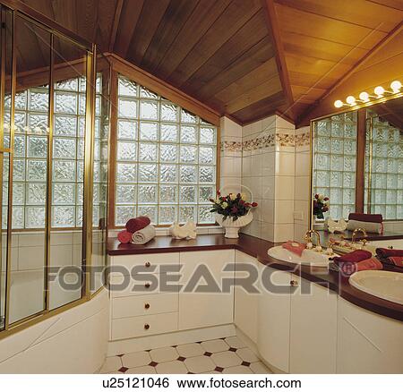 Stock Photograph - Hollywood-style light above vanity unit with double basins in modern bathroom with glass brick wall and wooden ceiling. Fotosearch
