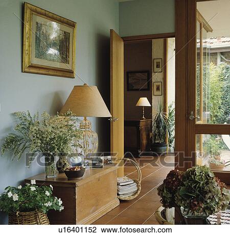 Informal flower arrangement and large lamp on pine chest in modern pale blue hall with terracotta floor tiles and glass door View Large Photo Image Stock Image - Informal flower arrangement and large lamp on pine chest in modern pale blue hall with terracotta floor tiles and glass door. Fotosearch