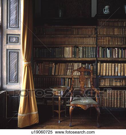 Stock Photography - Inlaid antique chair in front of bookshelves with leather-bound books in country study library. Fotosearch