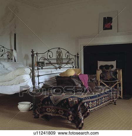 Kelim rug on stool below antique wrought bed with white linen in traditional bedroom View Large Photo Image Stock Photo - Kelim rug on stool below antique wrought bed with white linen in traditional bedroom. Fotosearch