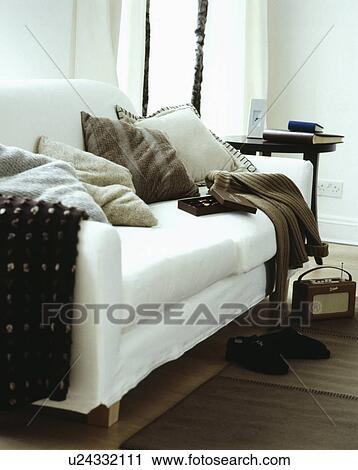 Stock Image - Knitted wool cushions and throws on sofa with white loosecover . Fotosearch