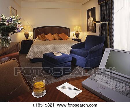 Laptop on table in hotel bedroom with blue velour armchair and lighted lamps on either side of the bed View Large Photo Image Stock Image - Laptop on table in hotel bedroom with blue velour armchair and lighted lamps on either side of the bed. Fotosearch