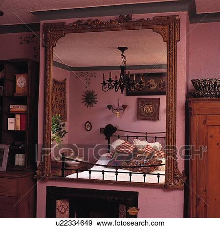 Large antique gilt mirror with reflection of pink bedroom with black iron bed and chandelier View Large Photo Image Stock Photo - Large antique gilt mirror with reflection of pink bedroom with black iron bed and chandelier. Fotosearch