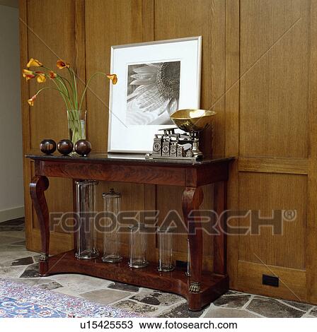 Stock Image - Large black+white photograph on panelled wall above old scales antique console table with glass cylinder vases. Fotosearch