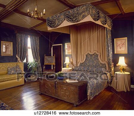Stock Photograph - Large country bedroom with polished wood floor and half-tester bed with blue and white patterned linen and curtains. Fotosearch