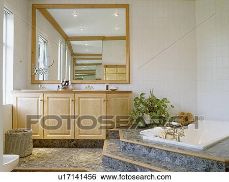 Large mirror above pale wood vanity unit in bathroom with marble steps to raised bath View Large Photo Image Stock Photograph - Large mirror above pale wood vanity unit in bathroom with marble steps to raised bath. Fotosearch