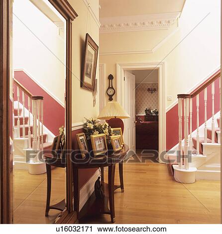 Large mirror and photographs on table in hall with wooden flooring and red dado on staircase View Large Photo Image Stock Image - Large mirror and photographs on table in hall with wooden flooring and red dado on staircase. Fotosearch