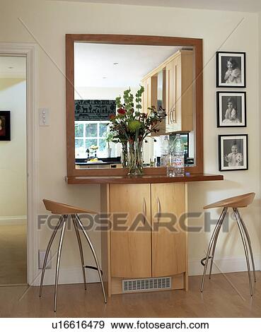 Large square mirror and black+white photographs on wall above small built-in cupboard and modern steel stools View Large Photo Image Stock Photo - Large square mirror and black+white photographs on wall above small built-in cupboard and modern steel stools. Fotosearch