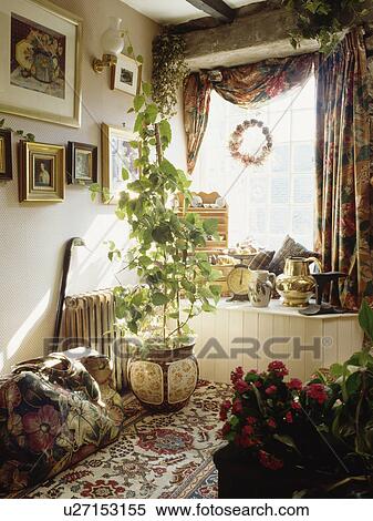 Stock Photography - Large tapestry bag beside houseplant in corner of cottage living room with floral curtains. Fotosearch