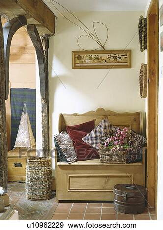 Stock Photo - Large willow basket beside old pine settle piled with cushions in country hall. Fotosearch