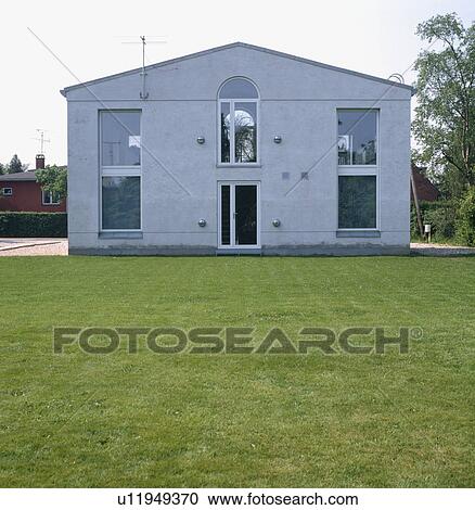 Stock Image - Lawn in front of modern grey house with large windows. Fotosearch