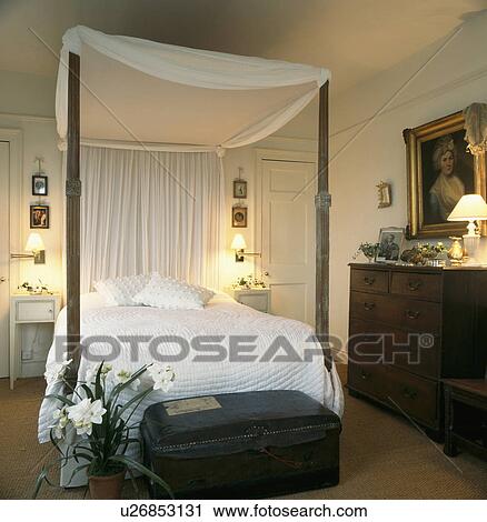 Lighted lamps in traditional bedroom with andtique chest and white canopy and quilt on four-poster bed View Large Photo Image Stock Image - Lighted lamps in traditional bedroom with andtique chest and white canopy and quilt on four-poster bed. Fotosearch