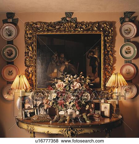 Stock Photo - Lighted lamps on console table below painting. Fotosearch