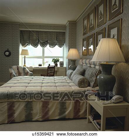 Lighted lamps on either side of bed in bedroom with grey+beige bedlinen and blind View Large Photo Image Stock Image - Lighted lamps on either side of bed in bedroom with grey+beige bedlinen and blind. Fotosearch